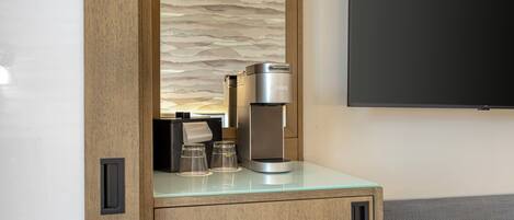 A modern kitchenette with a coffee machine, two glasses, and a small cabinet.