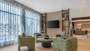 A modern living room with green upholstered chairs, a round coffee table, and a flat-screen TV mounted on the wall.