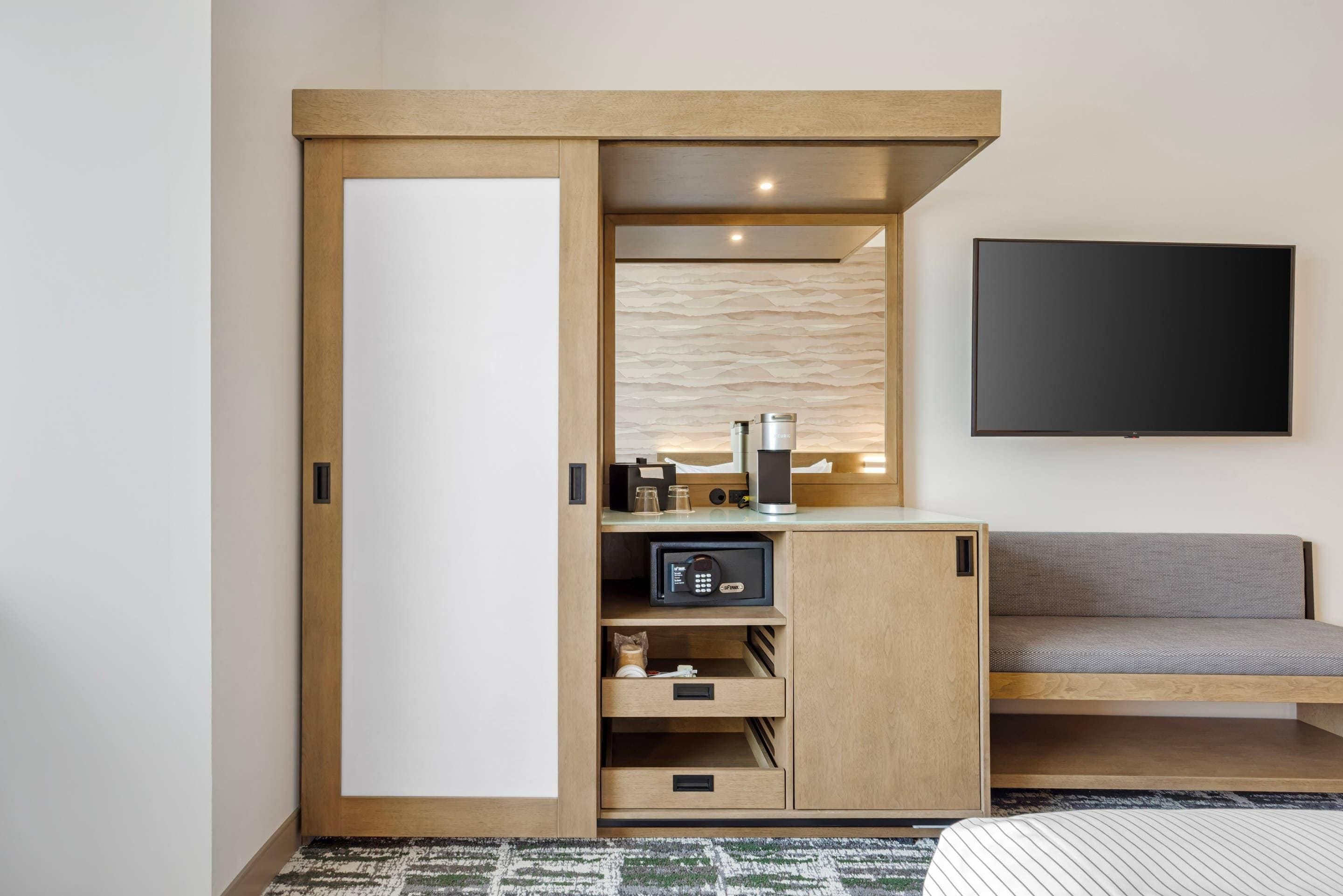 Una habitación moderna con armario empotrado, cafetera, televisor y sofá.