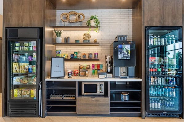 A self-service kiosk with refrigerated beverage dispensers, snack options, and a coffee machine.