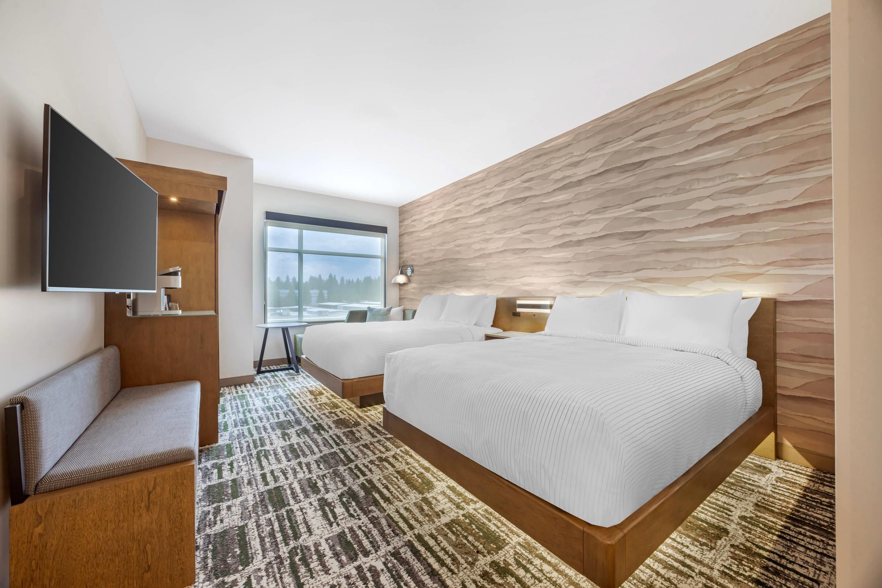 A modern hotel room with a large bed, a seating area, a flat-screen TV, and a view of the outdoors.