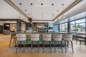A modern bar area with a long counter, multiple bar stools, and pendant lighting. - Cambria Hotel Bend - Mt. Bachelor (Bend)