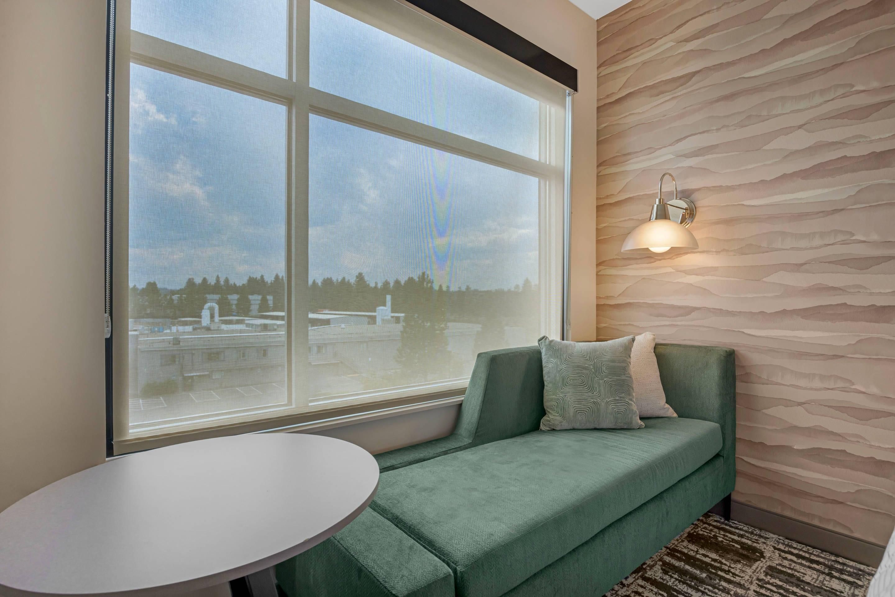 A room with a large window, a green sofa, and a round table.