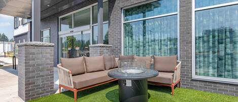 A modern outdoor seating area with a sectional sofa and a round table, surrounded by a well-maintained lawn.
