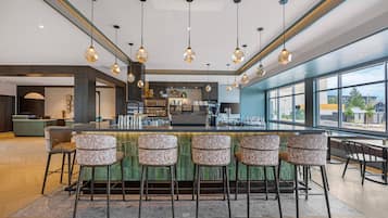 A modern bar area with a long counter, multiple bar stools, and pendant lighting.