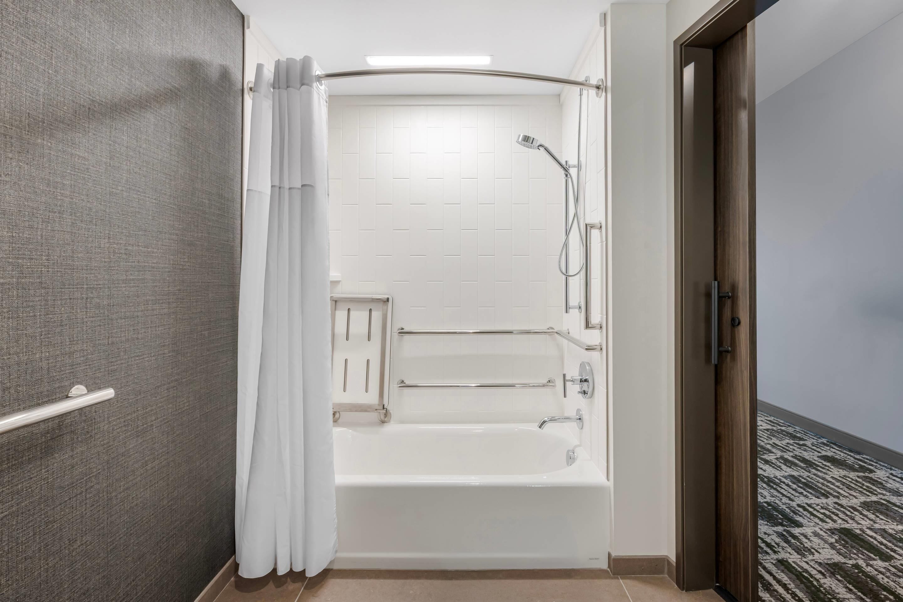Un baño moderno con ducha a nivel, barras de apoyo y una bañera blanca.