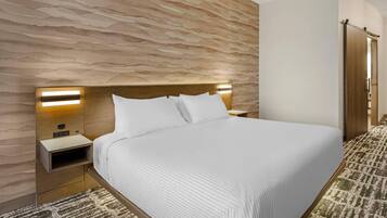 A hotel room with a large bed, a wooden headboard, bedside tables, and a patterned wall.