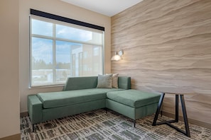 A modern living room with a sectional sofa, a patterned rug, a small round table, and a textured wall. - Cambria Hotel Bend - Mt. Bachelor (Bend)