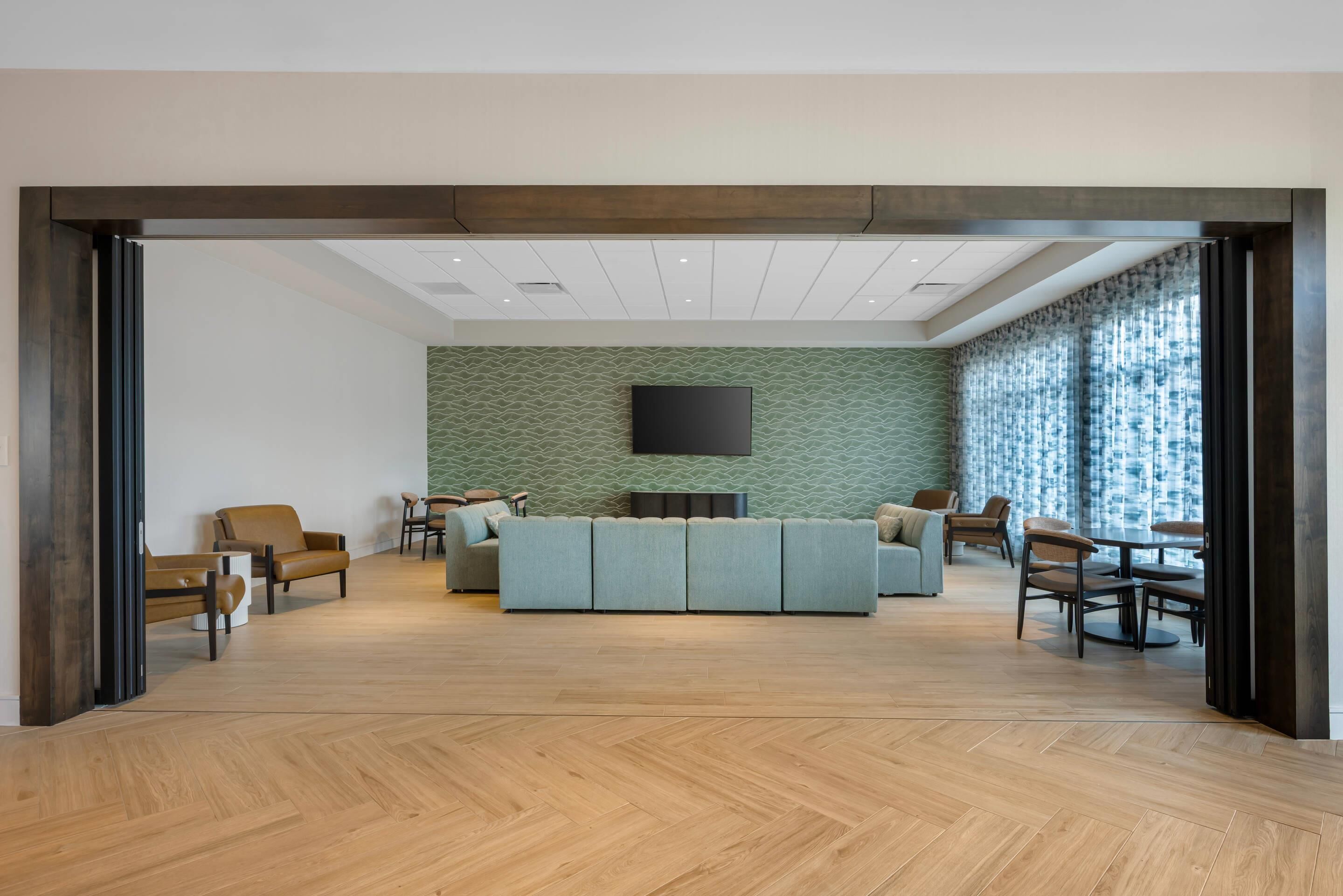 A modern living room with a herringbone wood floor, a sectional sofa, and a flat-screen TV mounted on the wall.