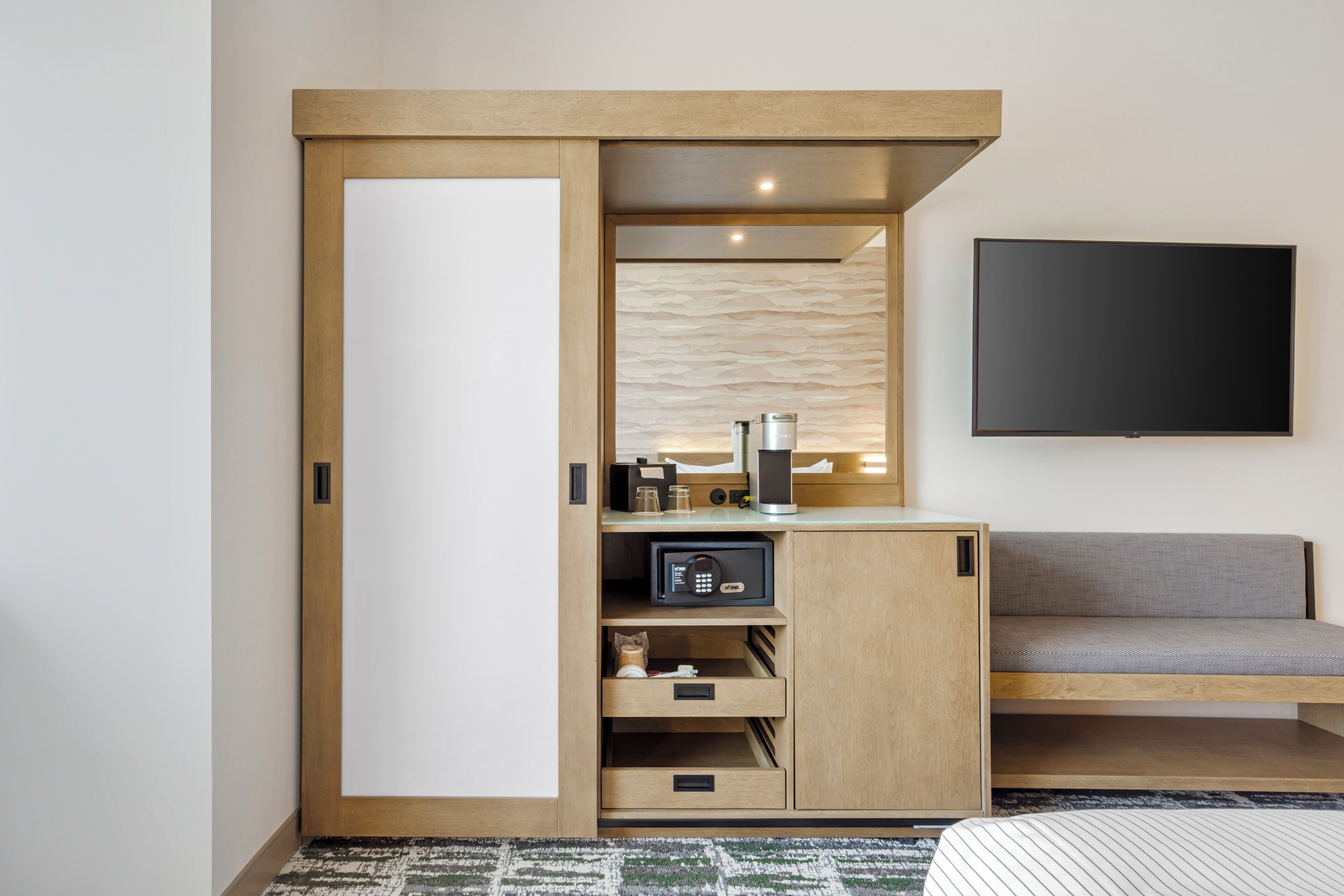 Habitación de hotel con armario de madera, sofá, televisión de pantalla plana y minibar.