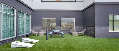 Un patio exterior moderno con césped artificial, una mesa de ping pong y dos sillones de mimbre.