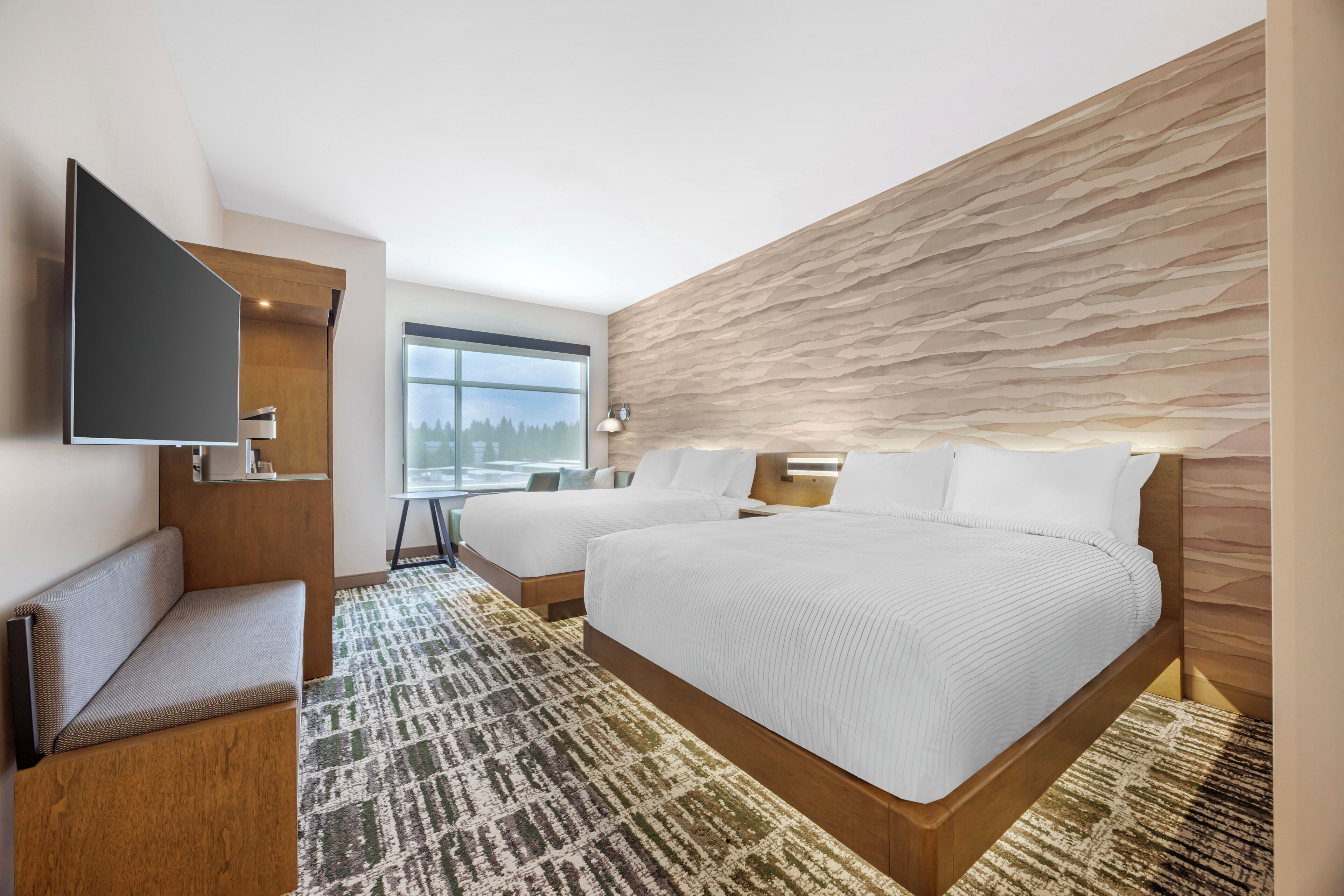 A modern hotel room with a large bed, a flat-screen TV, a seating area, and a view of the outdoors.