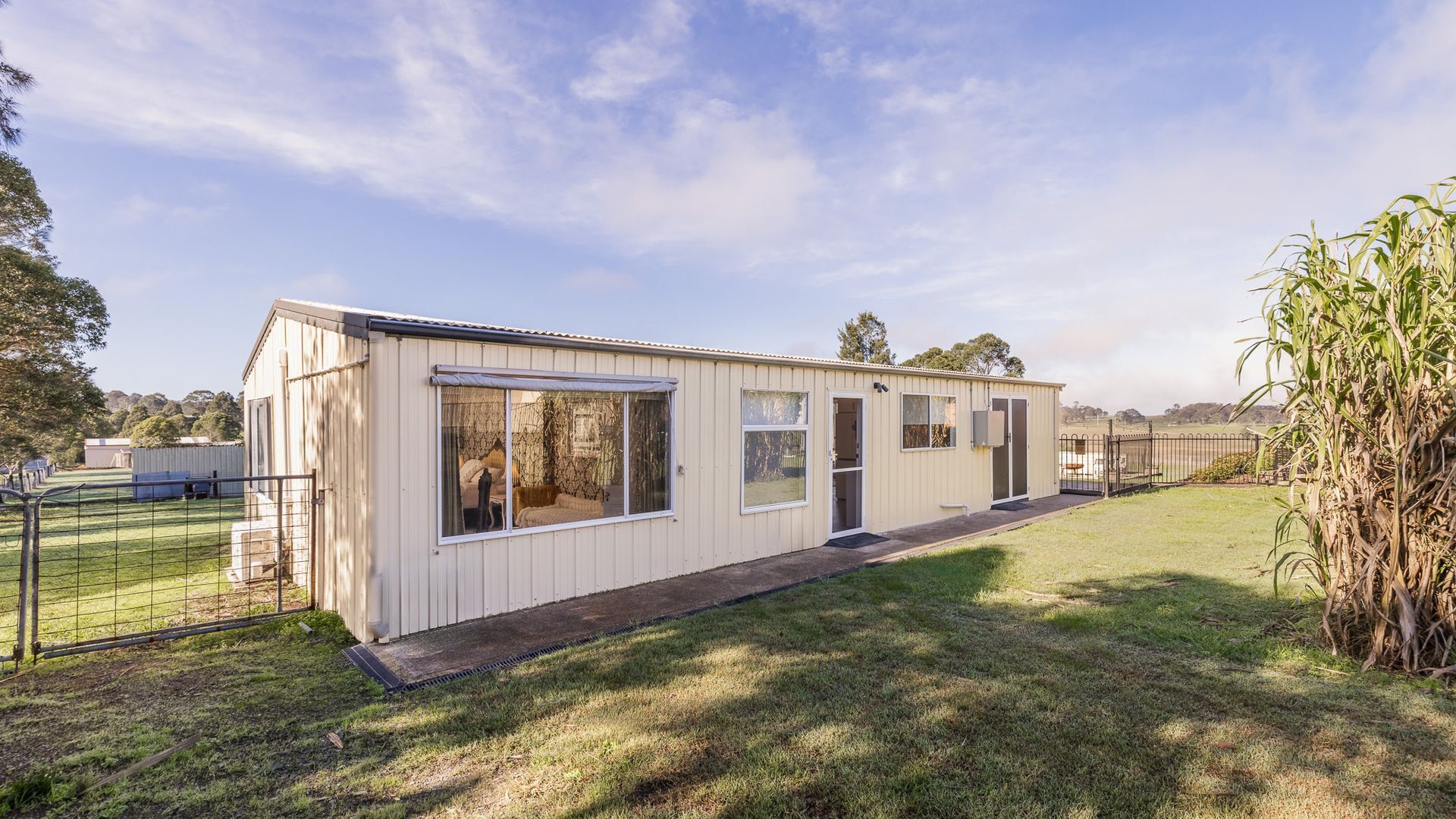 A single-story, light-colored mobile home with large windows, a door, and a small porch area.