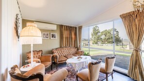 Ein Zimmer mit großem Fenster, einer Couch, Sesseln, einem Tisch und einer Lampe.
