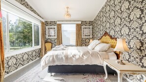 Quarto com uma cama grande, mesa de cabeceira, abajur e vista para o exterior.