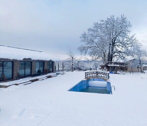 A snow-covered outdoor area with a pool, a glass-enclosed building, and a wooden deck. - Relax in Nature. Cozy Georgian resort with pool, stunning Views &Tranquility (Tskaltubo)