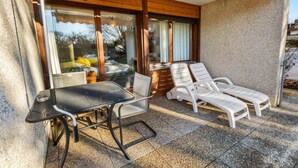 Une terrasse avec une table et des chaises, une chaise longue et une porte vitrée donnant sur une pièce.