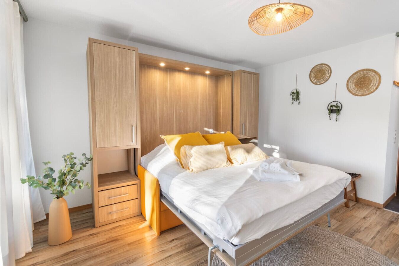 Une chambre à coucher comprenant un lit, une table de chevet, une armoire et une plante suspendue.