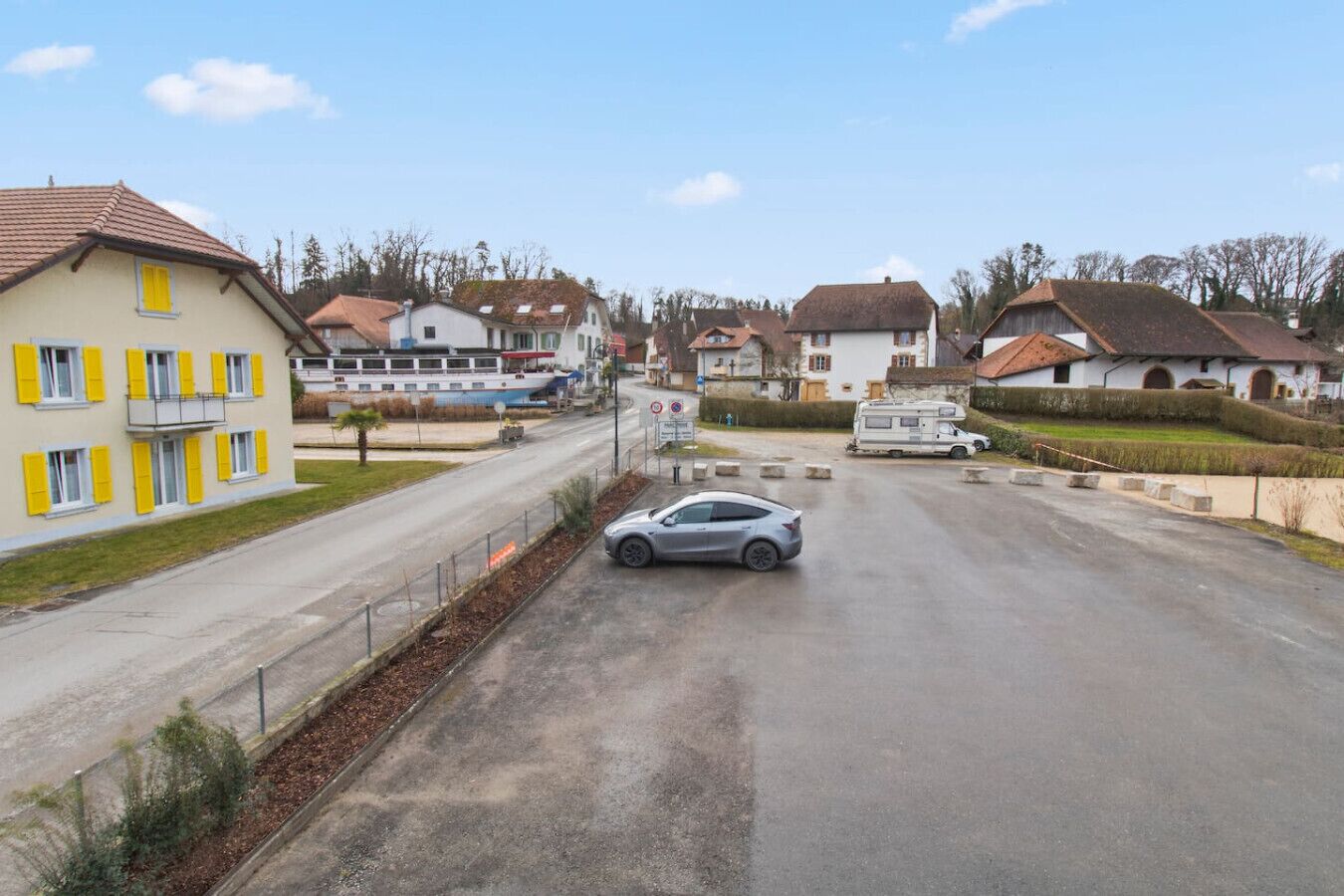 A residential street with houses, a parked car, and a boat.