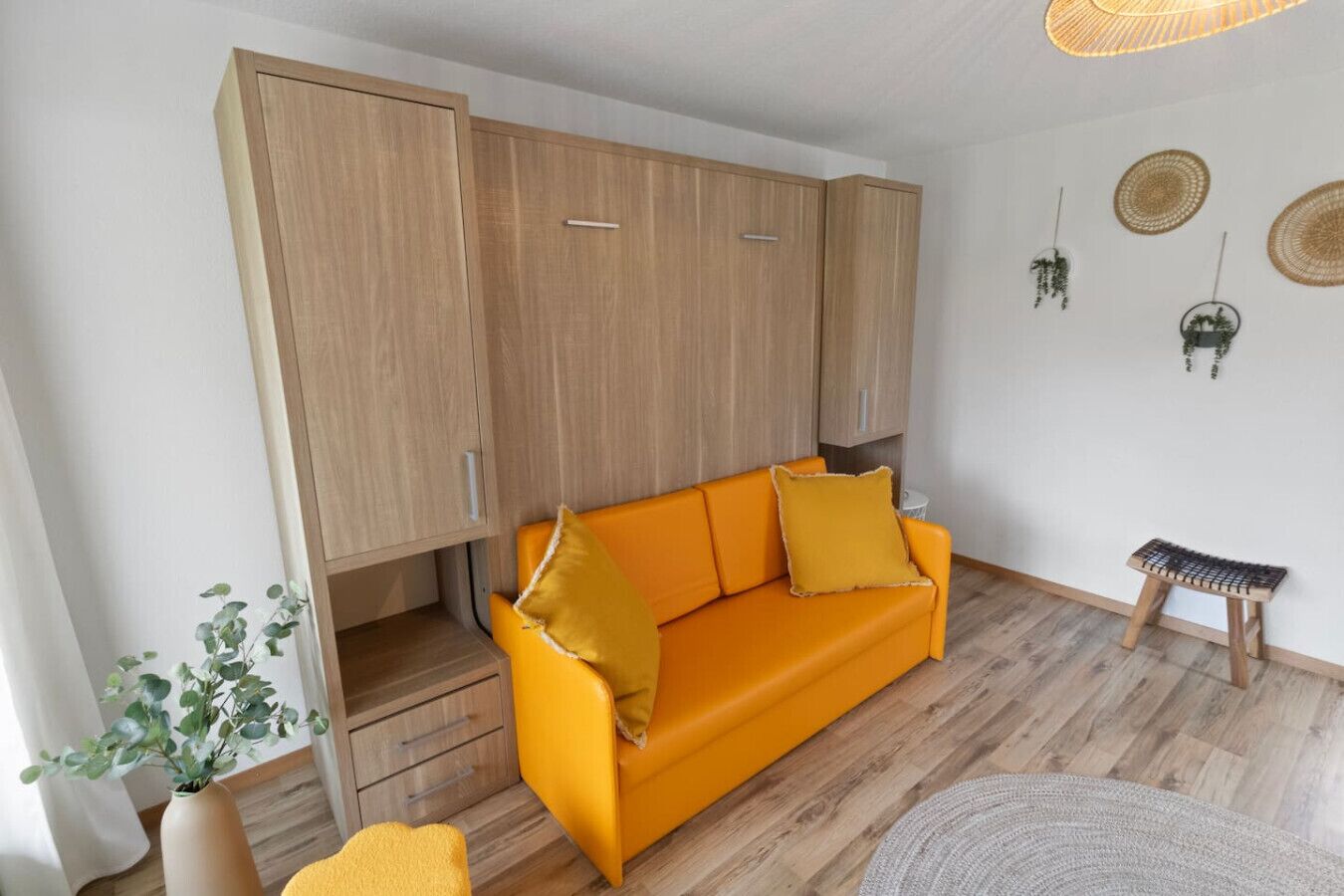 Une pièce comprenant un canapé, des meubles en bois, un petit tabouret et une plante.