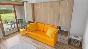 Une pièce comprenant une armoire en bois, un canapé jaune, une petite table ronde et une chaise en osier.