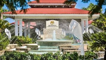 Un hotel con techo rojo, un letrero que dice 'The Tropical' y una fuente ornamental.