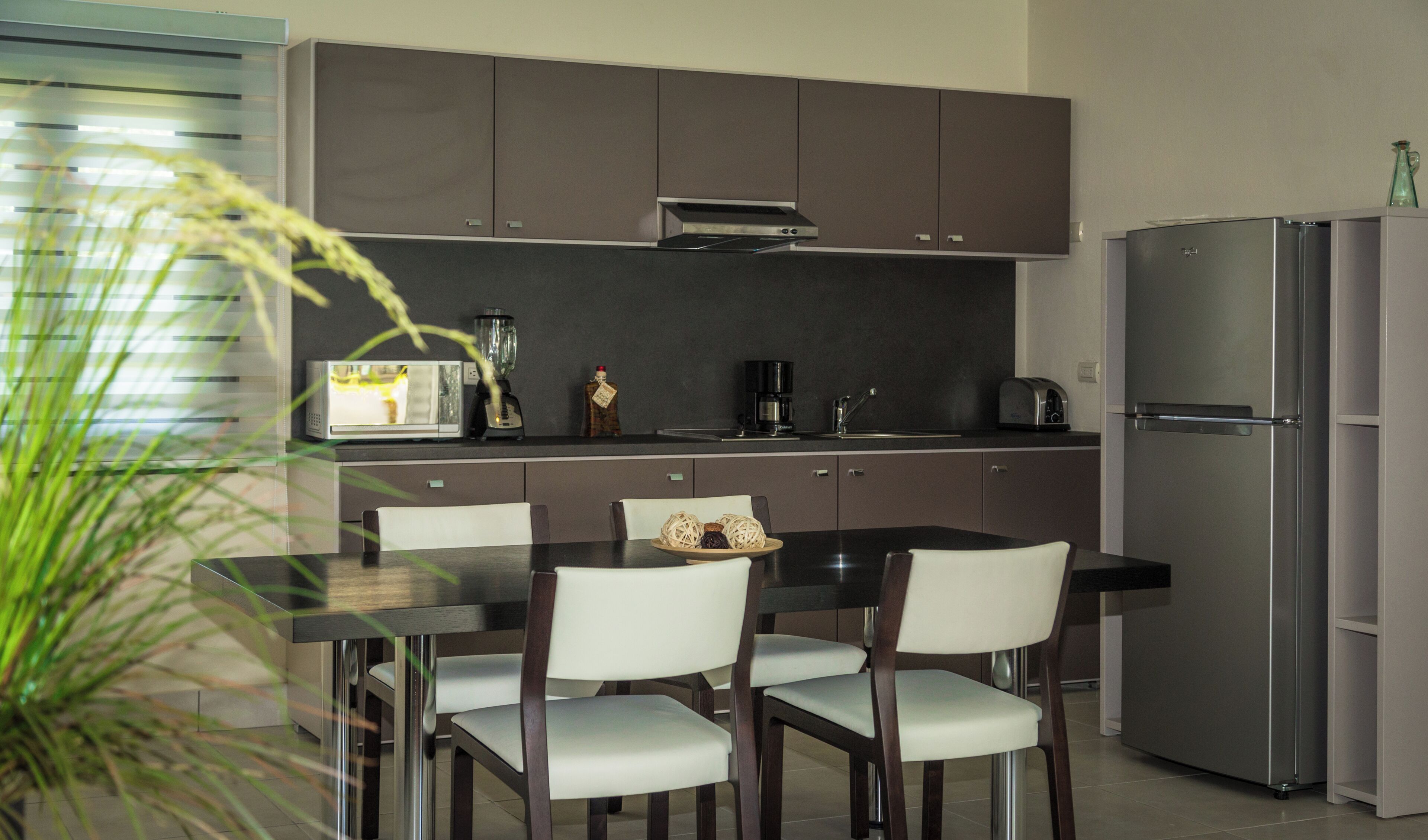 Una cocina moderna con armarios oscuros, un refrigerador de acero inoxidable, una mesa de comedor con sillas y una cafetera.