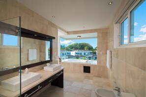 Ein modernes Badezimmer mit einem großen Spiegel, zwei Waschbecken, einer Badewanne und Blick auf eine Wohngegend.