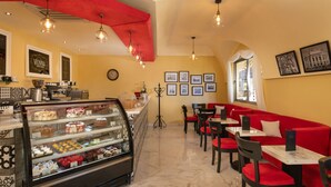 A café with a display case of pastries, red seating, and framed pictures on the walls. - Lifestyle Holiday Vacation Club (Puerto Plata)