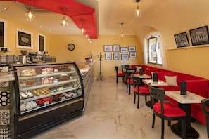 Una cafetería con una vitrina de pasteles, asientos rojos y cuadros en las paredes.