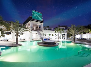 Nattebillede af et hotel med pool, palmer og et skilt for 'The Spot' hookah og vodka bar.