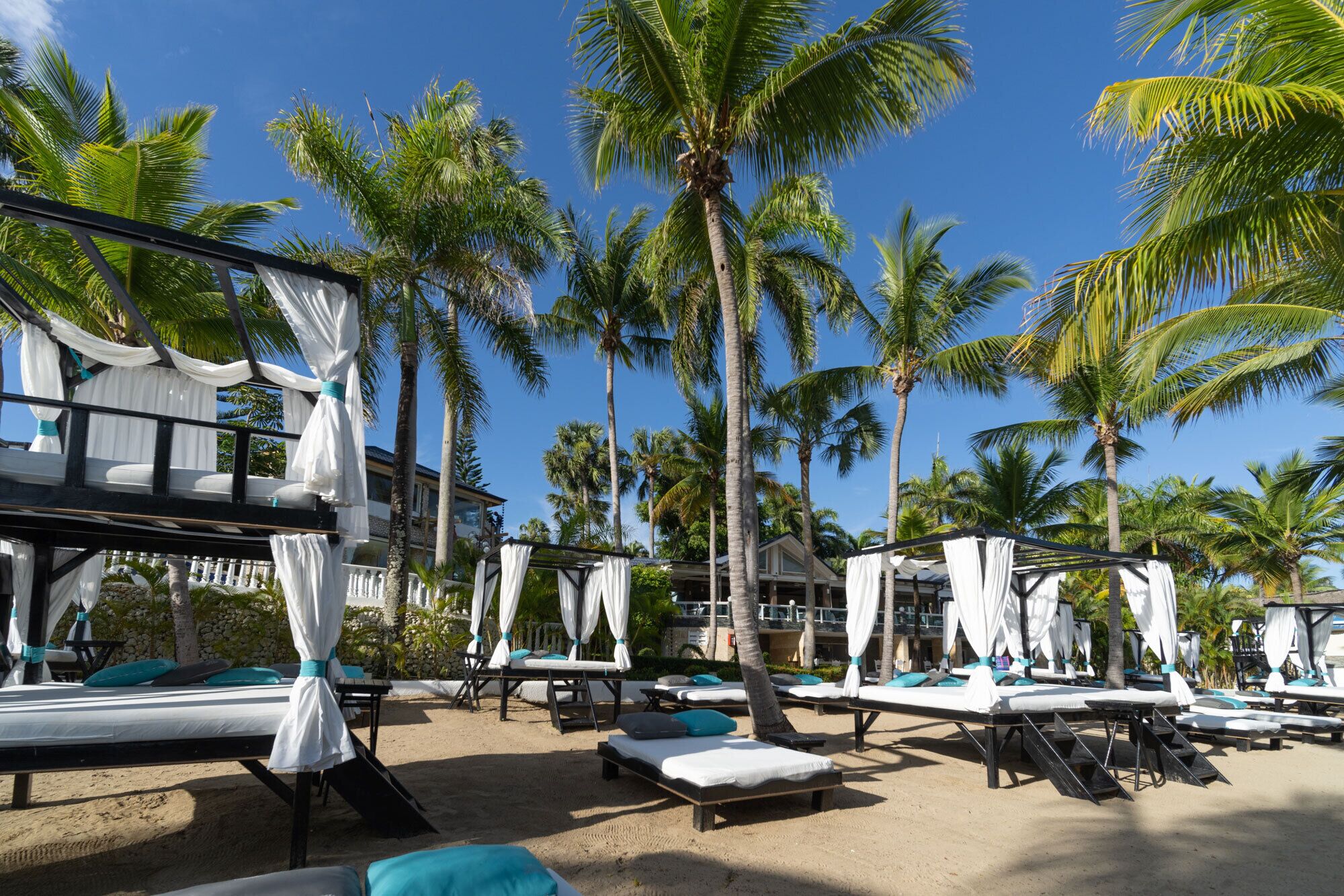 A beachside resort with multiple sunbeds, palm trees, and a building with a balcony.