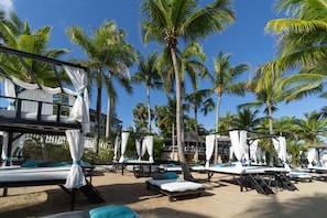 Resort à beira-mar com várias espreguiçadeiras, palmeiras e um edifício com varanda.
