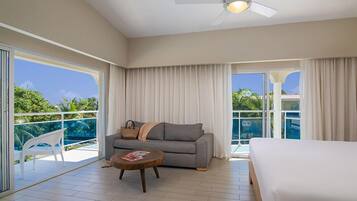 A hotel room with a bed, a sofa, a small table, and a balcony with a view of the ocean.