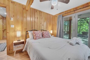 Ein schlafreicher Raum mit Holzvertäfelung, einem Bett, Nachttischen und Blick ins Freie.