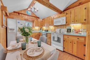 Ein Holzhütten-Interieur mit einem Esstisch, der für zwei Personen gedeckt ist, sowie einem Kühlschrank, einer Mikrowelle und einem Backofen.