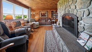 A cozy living room with a stone fireplace, wooden ceiling, and large windows.