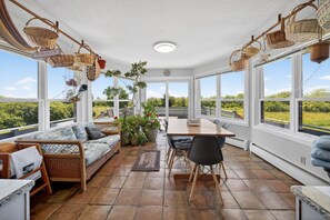 A sunlit room with wicker furniture, large windows, and a view of greenery. - Chace Point by the Ocean (Little Compton)