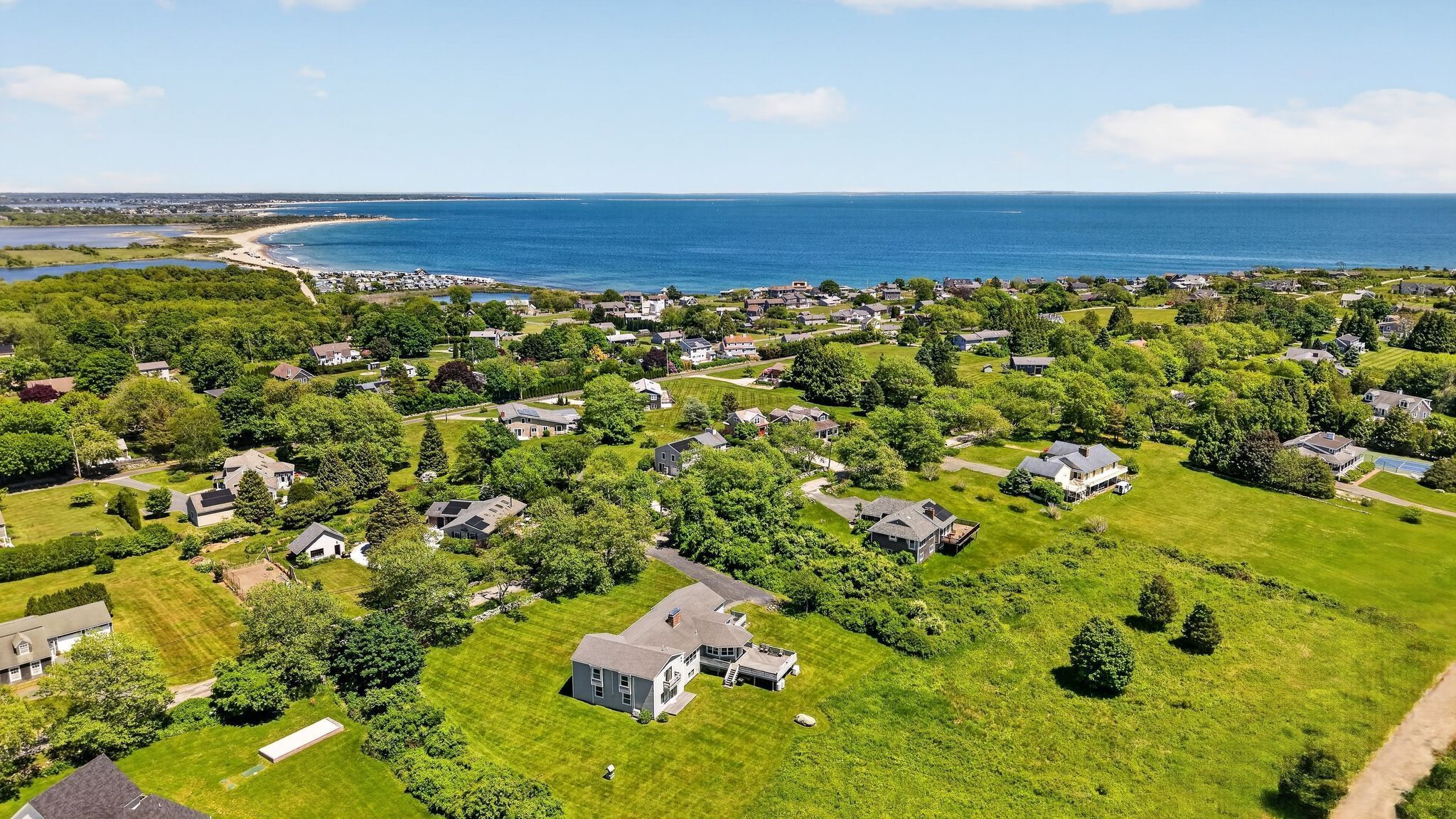 Ett bostadsområde med hus, grönskande gräsmattor och utsikt över havet.