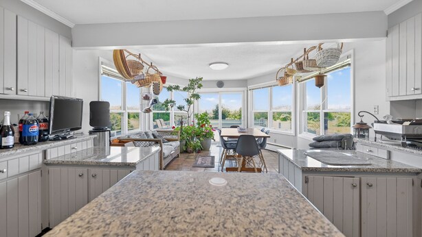 A kitchen with granite countertops, white cabinets, a dining area with a table and chairs, and large windows offering a view of the outdoors.