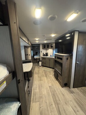 A compact RV interior with bunk beds, a kitchenette, and a TV.
