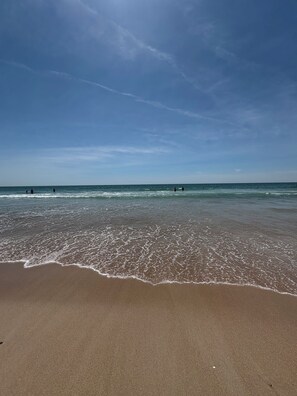 Une plage avec des vagues, un ciel dégagé et des personnes au loin.