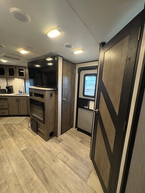 A compact RV kitchen with built-in appliances, a window with a view, and a door with a geometric design.