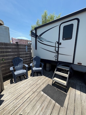 A recreational vehicle with a covered porch area, two Adirondack chairs, and a small table.