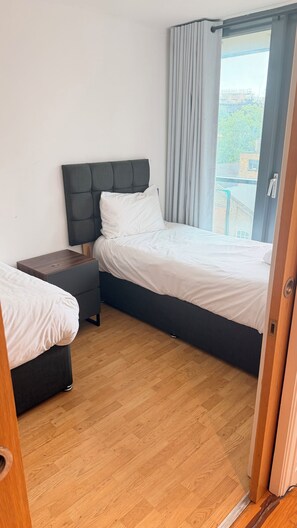 Ein Schlafzimmer mit einem Bett, einem Nachttisch, Holzboden und einem Fenster mit Vorhängen.