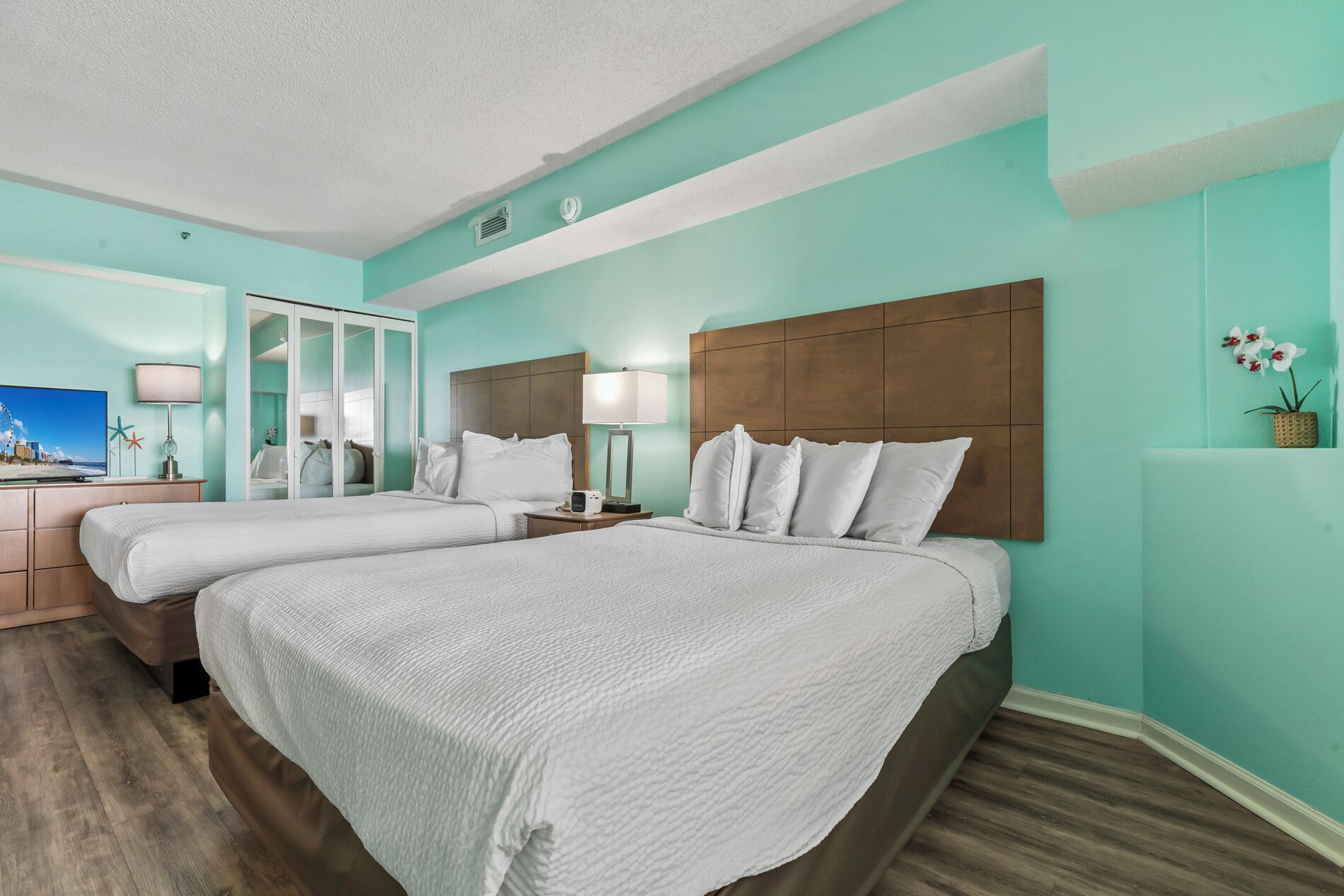 A hotel room with two beds, a TV, a desk, and a mirror.