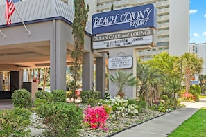 Schild für den Verkauf von Apartments direkt am Meer, mit einem Schild des Beach Colony Resort davor.
