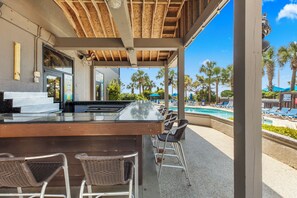 Un espace bar extérieur avec vue sur la piscine, des tabourets de bar et un plafond en bois.