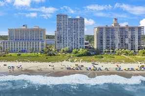 Ein Strandhotel mit mehreren Hochhäusern, einem Sandstrand und Meereswellen.