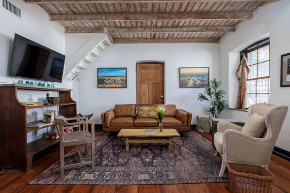 Una sala de estar con techo de madera, un sofá de cuero marrón, una mesa de centro de madera, un televisor y una estantería.